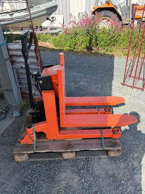 an orange forklift sitting on a pallet in front of a building