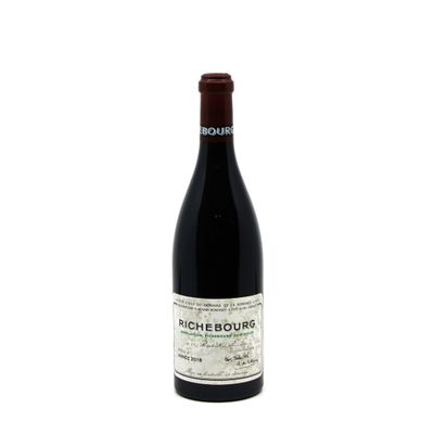the bottle of red wine is sitting on a white surface