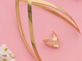 une broche en or et une paire de boucles d'oreilles posées sur un fond rose