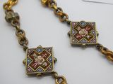 un gros plan d'un collier composé d'une chaîne en or et d'une perle rouge, bleue et verte