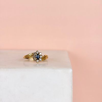 un gros plan d'une bague en or sertie d'un diamant bleu, posée sur un bloc blanc