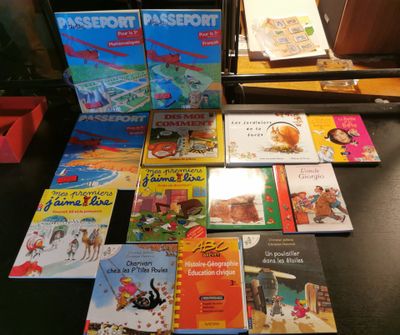 Plusieurs livres pour enfants sont posés sur un bureau, devant une lampe.