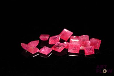 pink crystals are scattered on a black surface in the dark