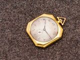 une petite montre de poche en or posée sur un tissu marron