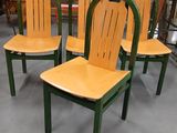 Quatre chaises en bois sont alignées dans une pièce, avec un tableau accroché au mur derrière elles.