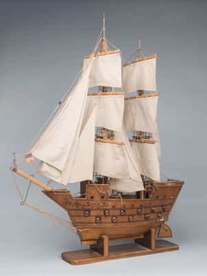 wooden model of a tall sailing ship with white sails on a wooden stand