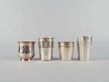 quatre tasses en argent sont alignées les unes à côté des autres sur une surface blanche