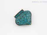 a close up of a turquoise and gold broochle on a white surface