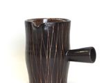 a black cup with a brown handle on a white surface