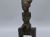 une petite statue en bois représentant une femme assise sur un tabouret