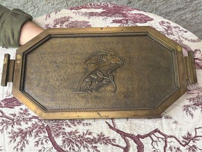 someone is holding a brass plate with a picture of a bird on it