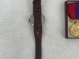 an image of a watch and medal laying on a white surface