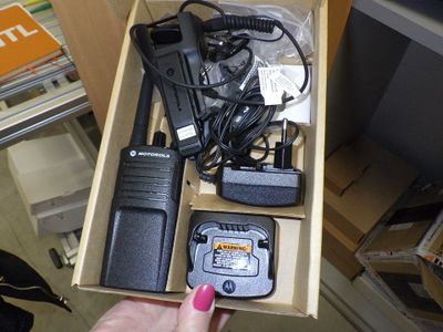 une personne tenant une boîte contenant deux talkies-walkies et un chargeur
