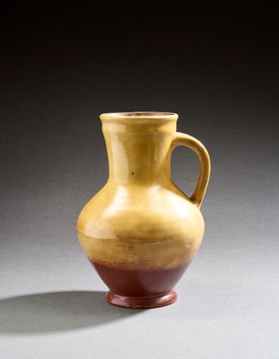 un vase jaune et rouge posé sur une surface grise, sur fond noir