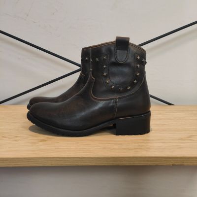 des bottes en cuir marron ornées de clous, posées sur une étagère en bois devant un mur blanc