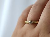 a woman ' s hand holding a gold ring with a diamond on it