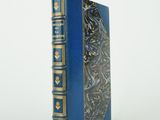un vieux livre bleu aux bords dorés posé sur une surface blanche