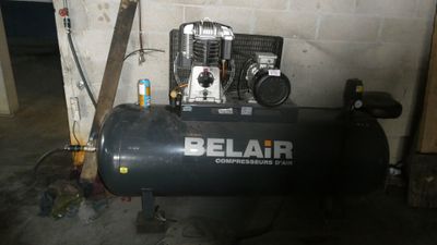 un compresseur d'air noir posé dans un garage, près d'un mur