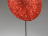 a red sculpture on a black stand with a gray background