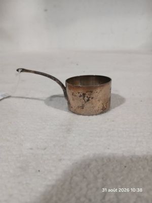 une petite casserole en métal avec une poignée, posée sur une table