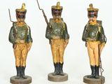 trois figurines de soldats en uniformes verts et jaunes, posées sur des socles en bois