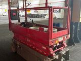 a red scissor sitting in a warehouse with a white car in the background