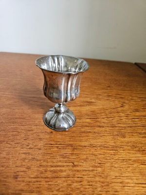 une coupe en argent posée sur une table en bois, avec un mur blanc en arrière-plan