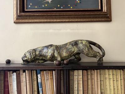 a statue of a cat on a book shelf in front of a painting