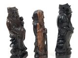 three carved figurines of people in various poses on a white surface