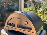 an outdoor pizza oven sitting on top of a table in front of a house