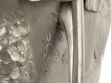 a silver vase with flowers on it on a white surface