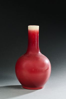 un vase rouge posé sur une table, sur fond noir
