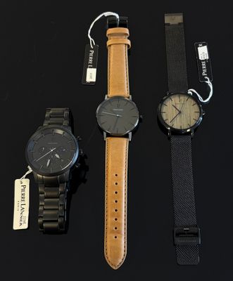 trois montres sont posées sur une surface noire, accompagnées d'une étiquette de prix
