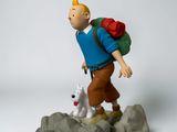 figurine of a man with a backpack and a dog on top of a rock