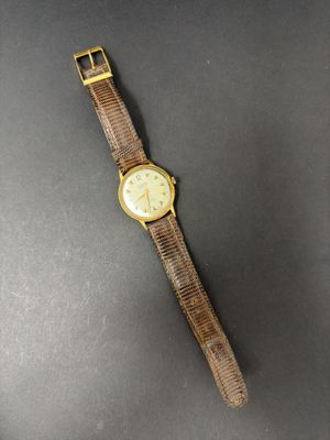 a gold watch with a brown strap on a black surface