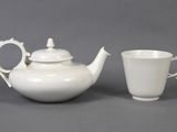 une théière blanche et une tasse posées l'une à côté de l'autre