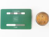 a small coin next to a green card on a white surface