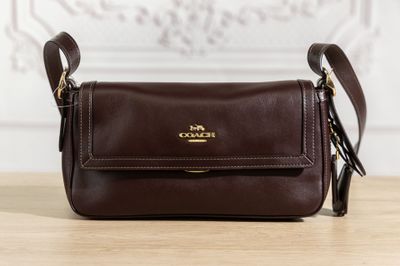 un sac à main marron de la marque Coach posé sur une table en bois