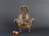 un vase en bronze orné d'un oiseau, avec une noix posée à ses pieds