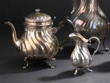 trois théières en argent et une cafetière en argent posées sur une table
