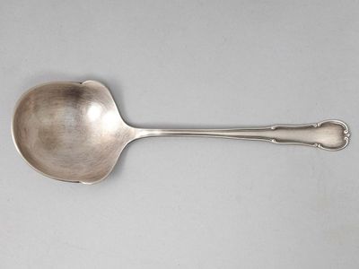 une cuillère ancienne en argent à long manche posée sur une surface blanche