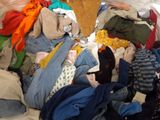a pile of clothes on a bed with a person standing next to it