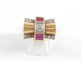 une photo d'une bague sertie d'un diamant et d'un rubis posée sur une surface claire