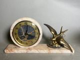 une horloge ornée d'un oiseau et une figurine d'oiseau posée sur un socle en marbre