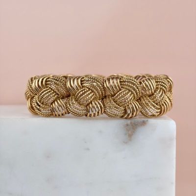 a close up of a gold braided bracelet on a marble block