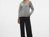 a woman in a grey sweater and black pants stands in front of a white background