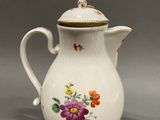 a white pitcher with flowers on it on a gray surface