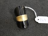 une bague noire et dorée posée sur une surface noire, avec une étiquette de prix