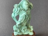 statue d'une femme tenant un poisson, posée sur un socle, sur fond gris
