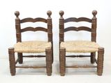 pair of antique wooden chairs with woven seats against a white wall